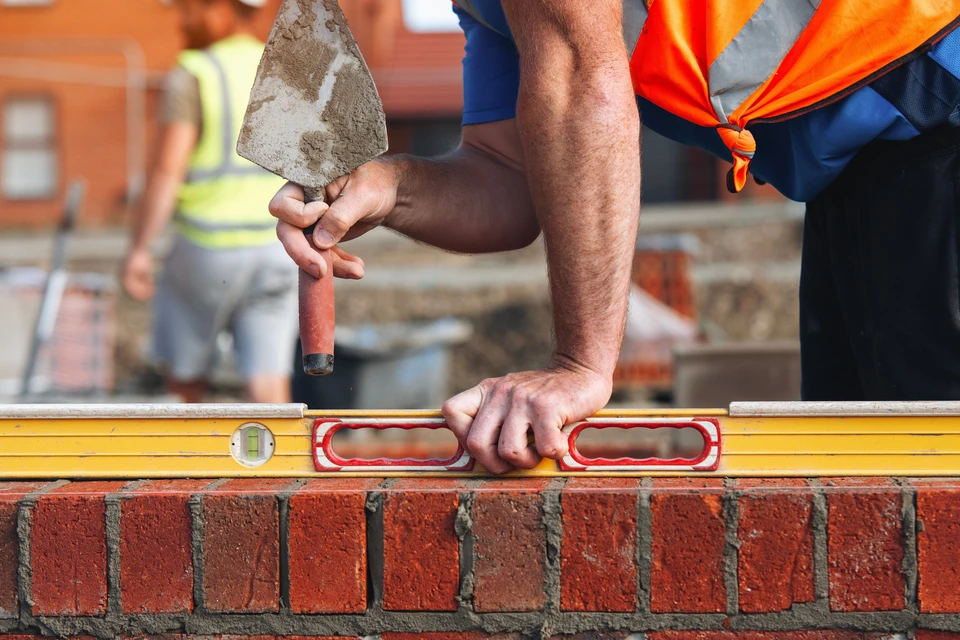 Un maçon qualifié vérifie le niveau de briques fraîchement posées sur un chantier de construction à la lumière du soleil de l'après-midi
